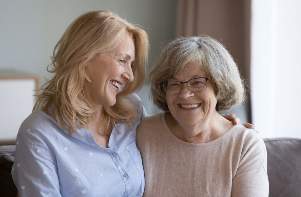 An adult hugging their smiling older parent during a visit in assisted living.